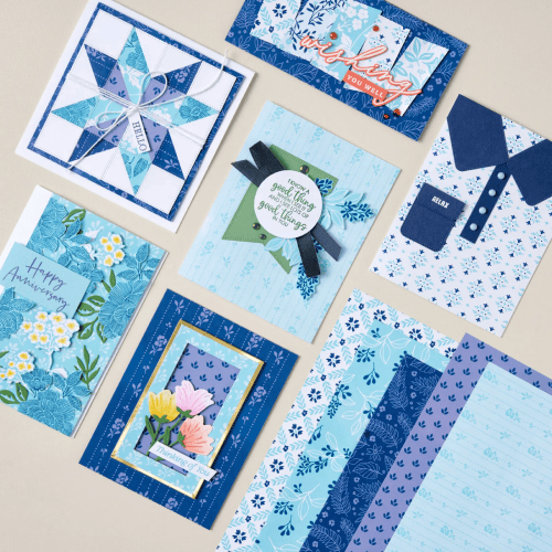 A collection of handcrafted greeting cards and patterned papers in various shades of blue, featuring floral designs, geometric patterns, and a 'Happy Anniversary' message.