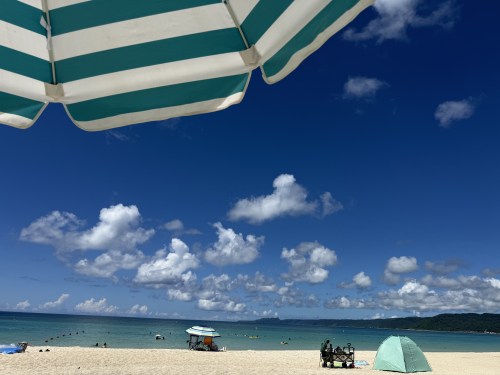 ビーチの景色、青い空と白い雲、パラソルの下からの眺め、砂浜に人々がいる