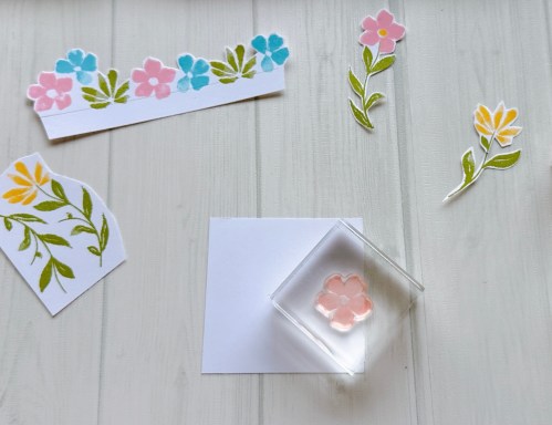 手作りの花柄のスタンプとカラフルな花のカットアウトが周囲に配置されたホワイトカード