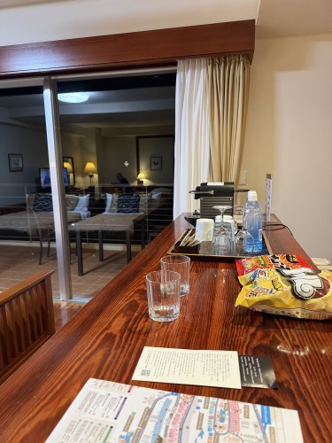 ホテルの部屋のカウンターに飲み物とスナックが置かれ、外にバルコニーとリビングエリアが見える