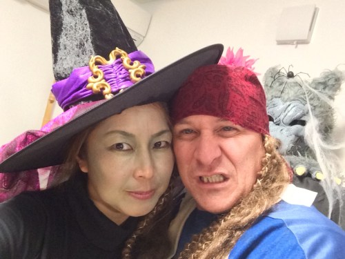 ハロウィンの仮装をした男女が顔を寄せ合っている。女性は紫の魔女の帽子をかぶり、緑色のメイクをしている。男性は赤いバンダナを巻き、怒った表情をしている。